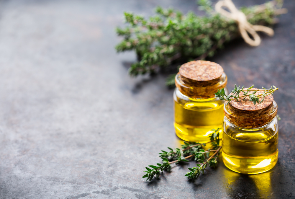 thyme oil in two glass jars next to bunch of thyme